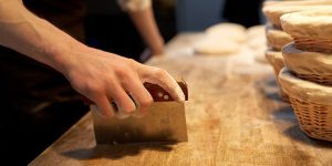 Baker portioning dough with bench scraper at bakery